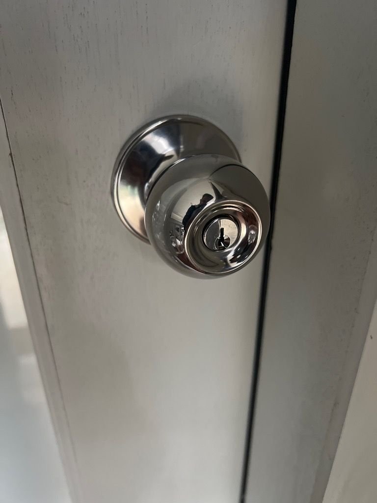 Close-up of a metal door knob with an integrated keyhole on a white wooden door.