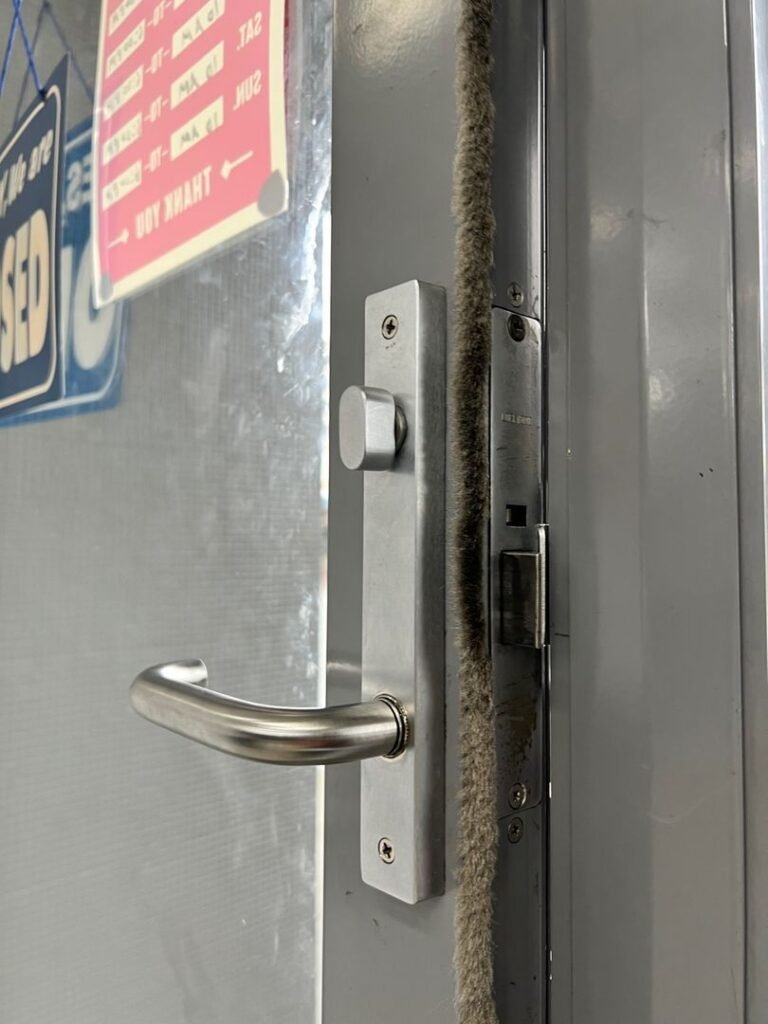 Newly installed stainless steel door lock handle on a metal door with visible business hour signs in Dandenong office.