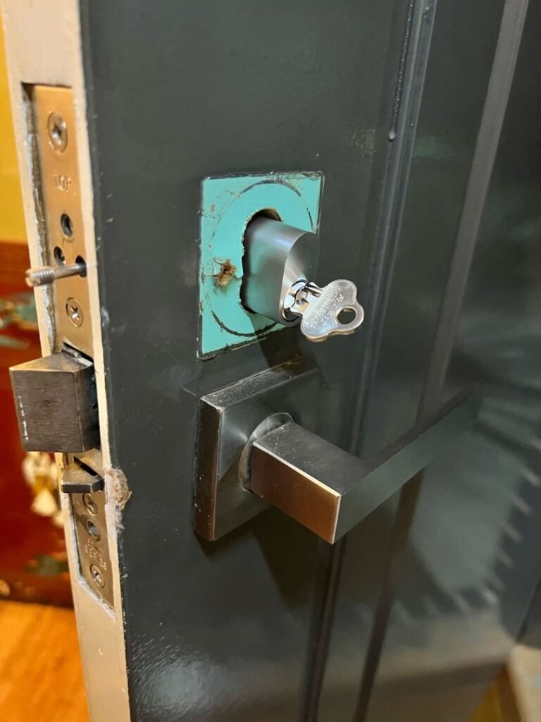 New lock barrel installed on dark-colored door with modern metallic handle and key inserted.