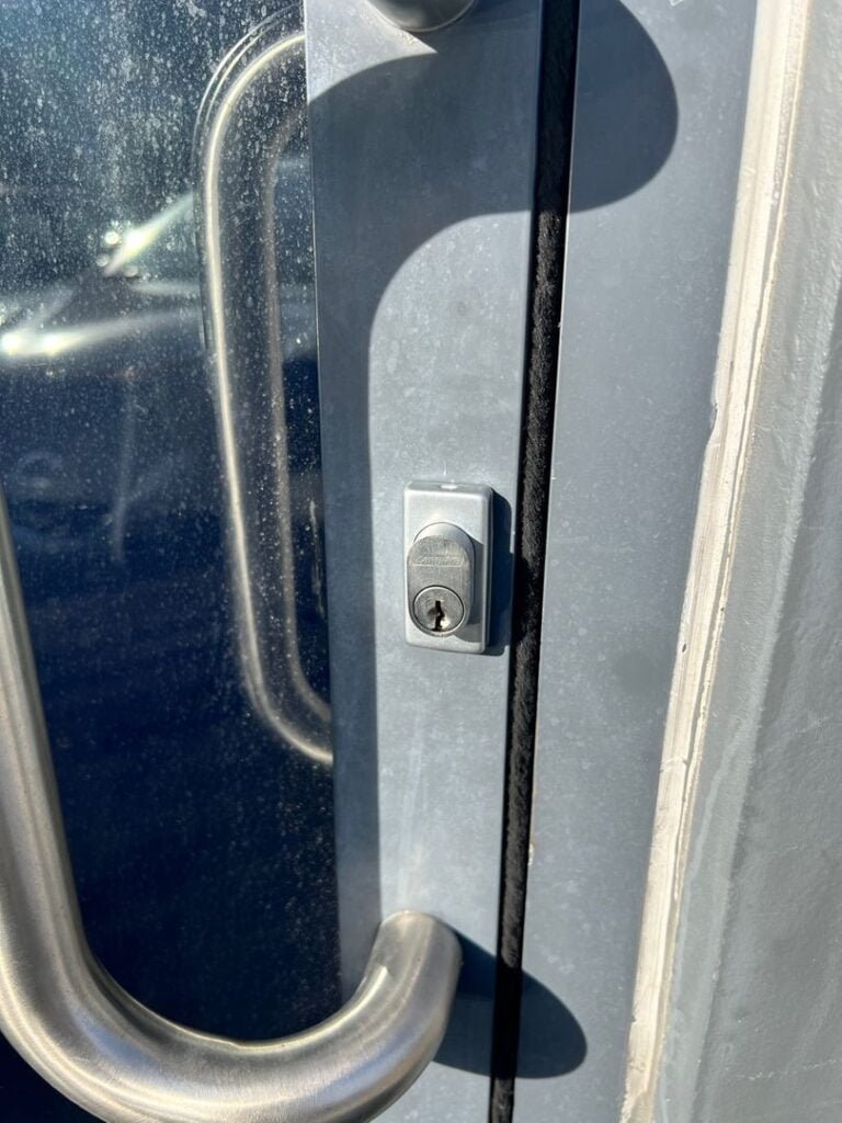 Close-up of a new lock barrel installed on a metal and glass office door with stainless steel handles.