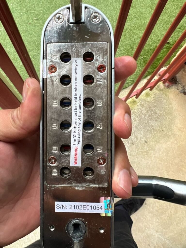 Close-up of a keypad entry lock showing numbered buttons, warning label, and serial number.