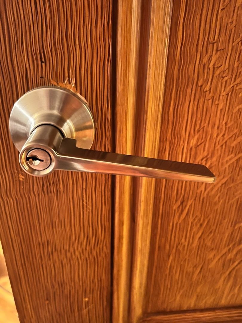 Close-up of a metallic door handle with a keyhole on a textured wooden door.