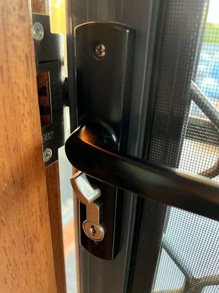 Close-up view of a black metal door lock on a wooden frame with a mesh screen in the background.