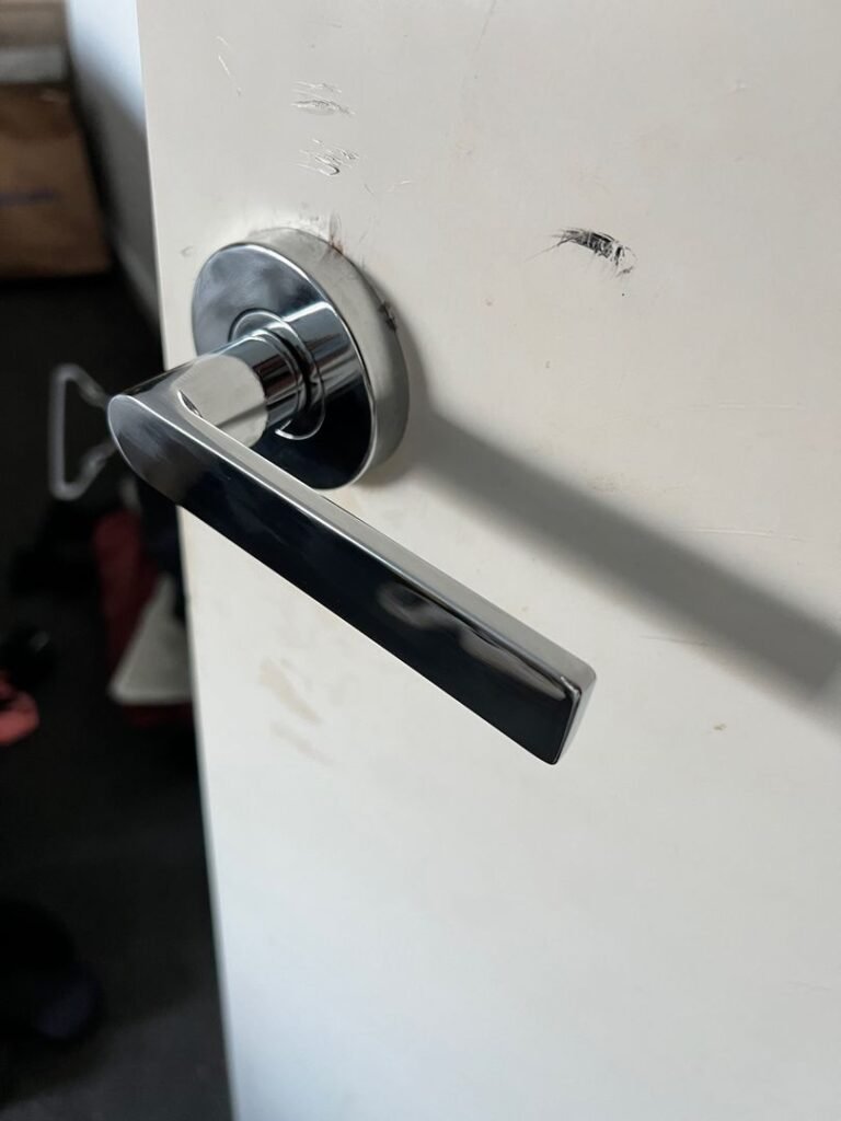 Newly installed modern metallic door handle on a white bedroom door with visible scratches around the installation area.