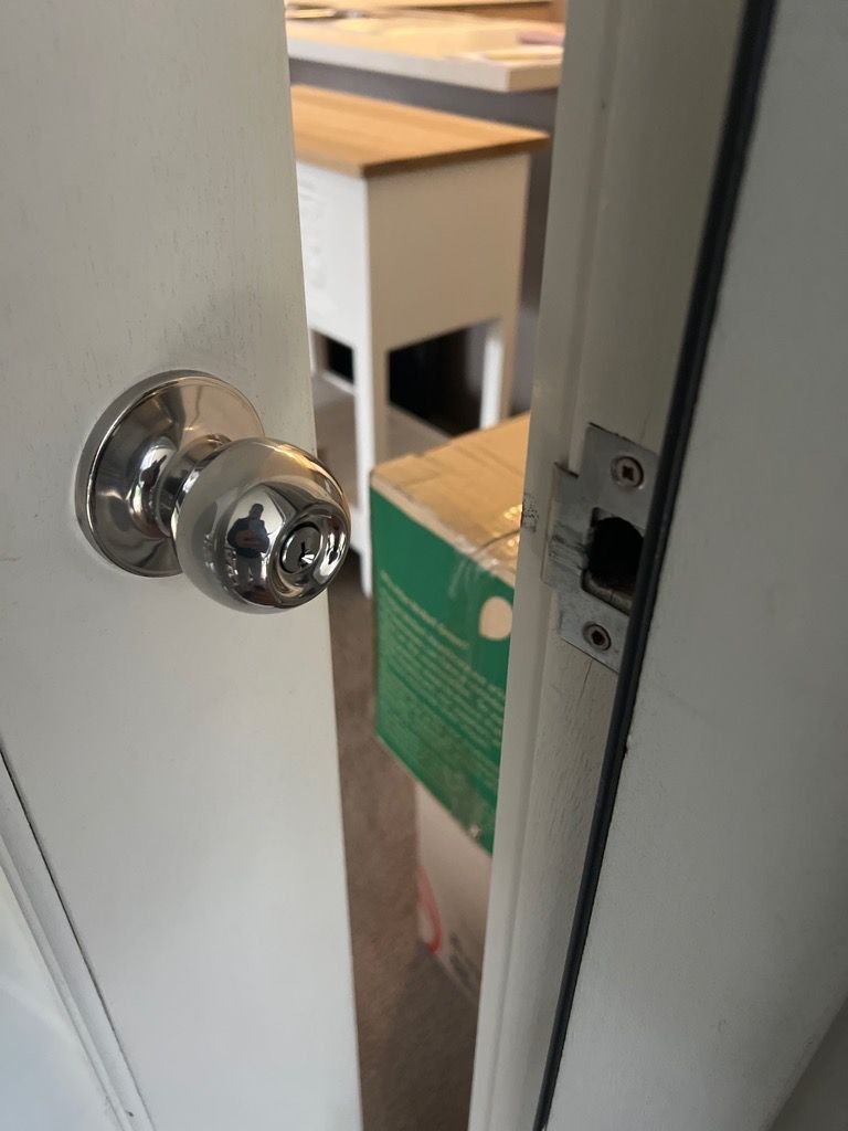 Partially open white door with silver knob and visible latch mechanism in a residential setting.