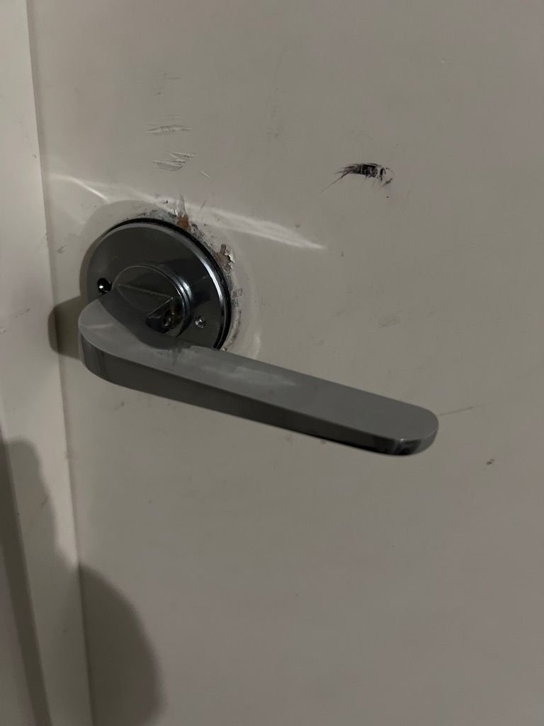 A close-up of a newly installed metallic lever door handle on a white door with visible marks around the installation area.