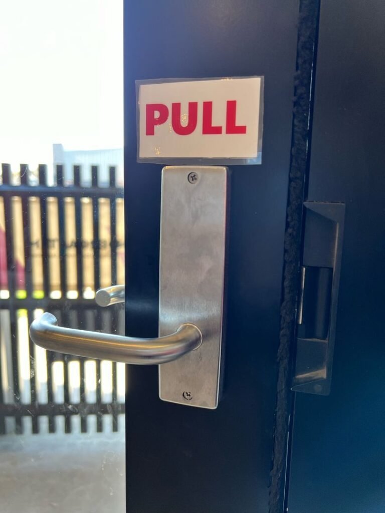 Close-up of a metallic door handle with a PULL sign above it on a black door, with an industrial area visible in the background.