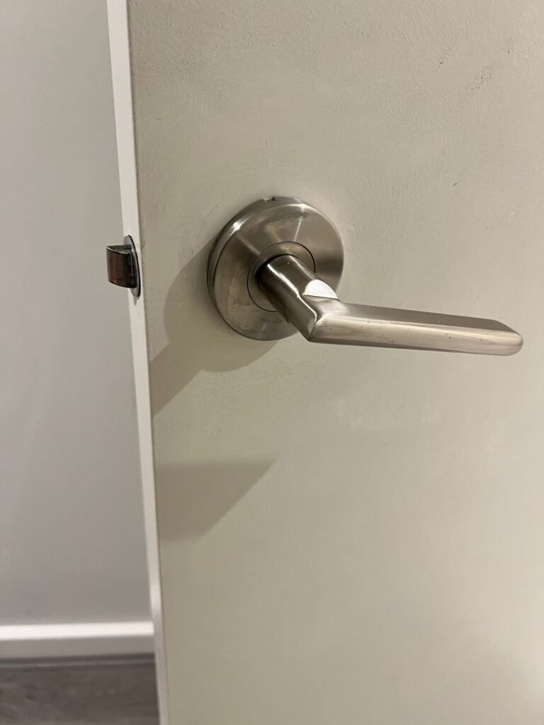 Close-up of a newly installed brushed metal privacy door handle on a white door.