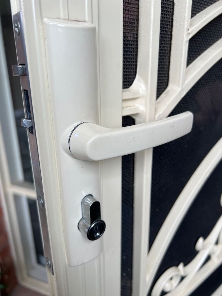 Close-up image of a security screen door lock with a white handle and keyhole.