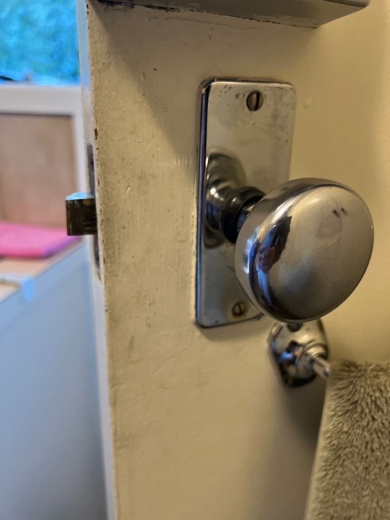 Close-up of a new metallic door knob installed on a white door with background elements including part of a room and window.