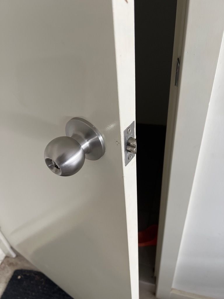 A white door with a silver doorknob is partially open, revealing a dark room inside.