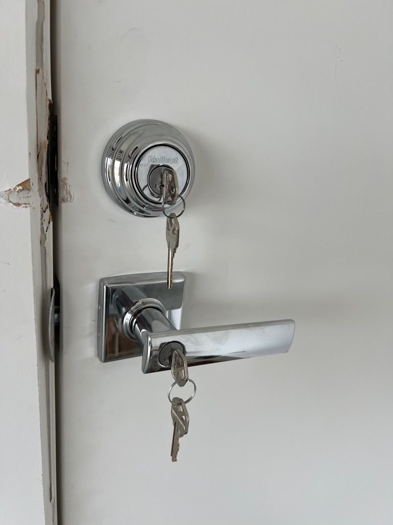 White door with chrome Kwikset deadbolt and entrance leverset, both with keys inserted.