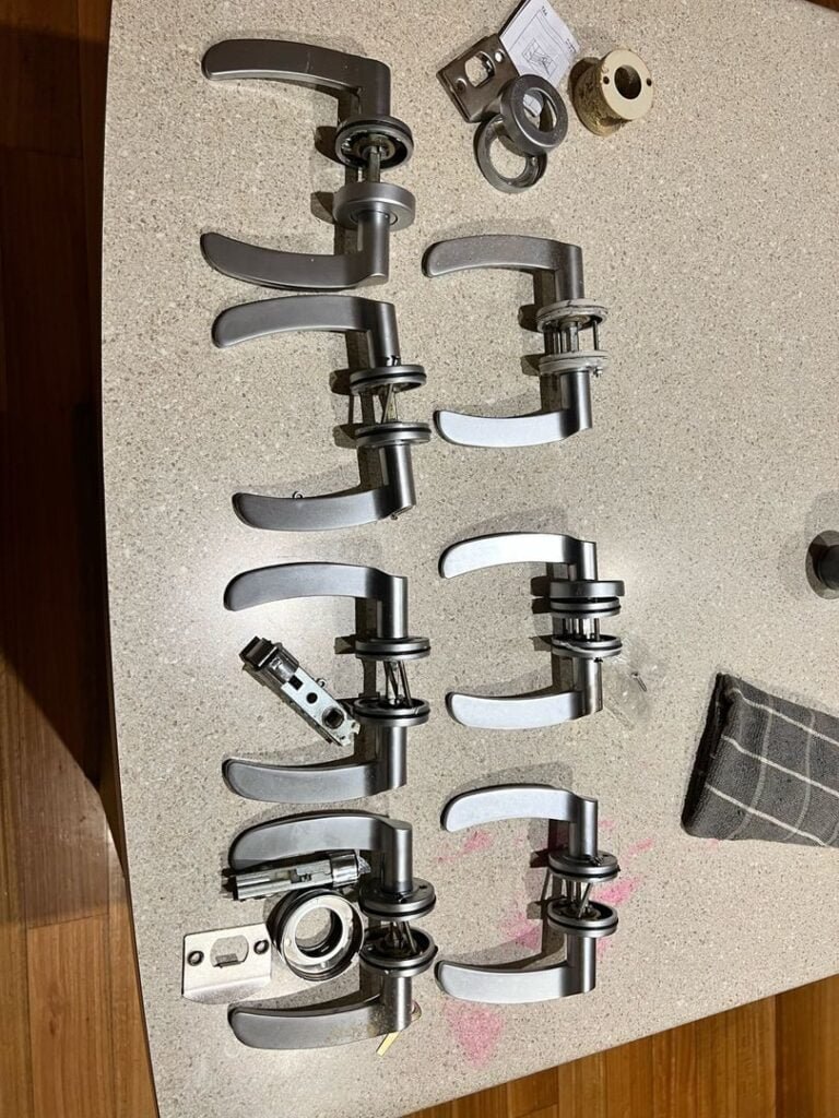 Several silver door levers and hardware parts laid out on a countertop, indicating preparation for a lock change.