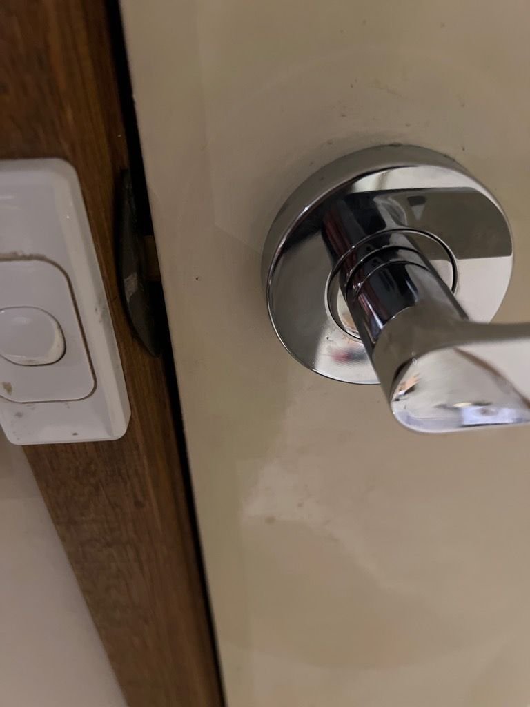 Close-up of a chrome leverset door handle and adjacent light switch on a wooden frame.