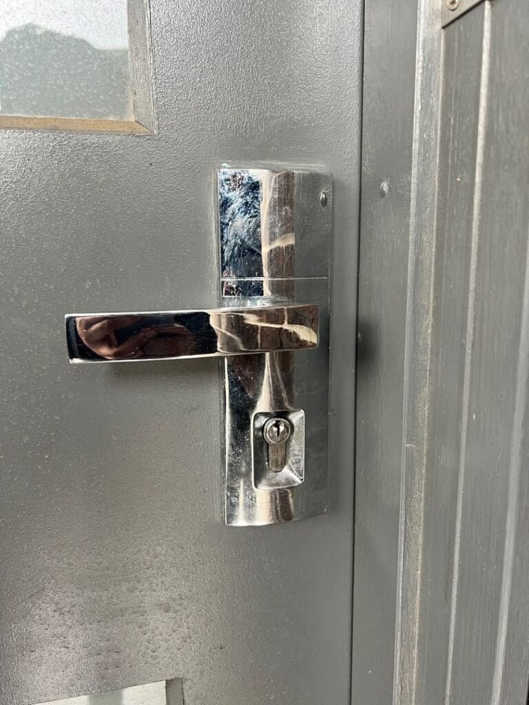 Close-up view of a metallic door lock on a grey door with visible handle and keyhole.