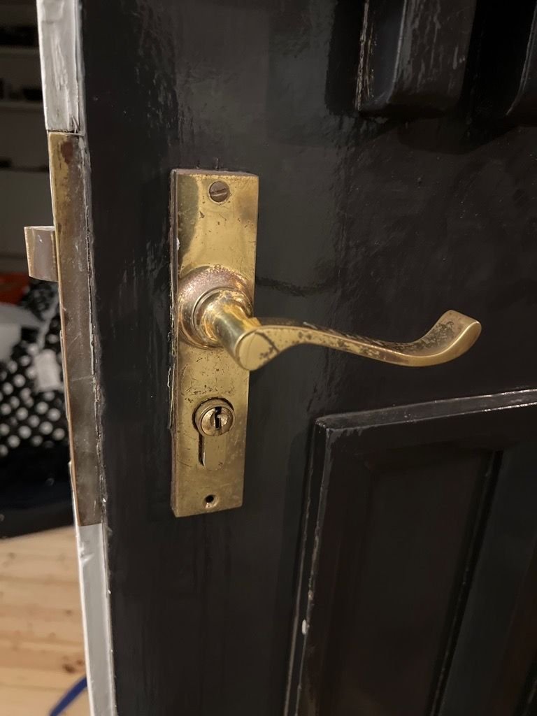 Old mortice lock with a key stuck in the barrel on a black-painted door.