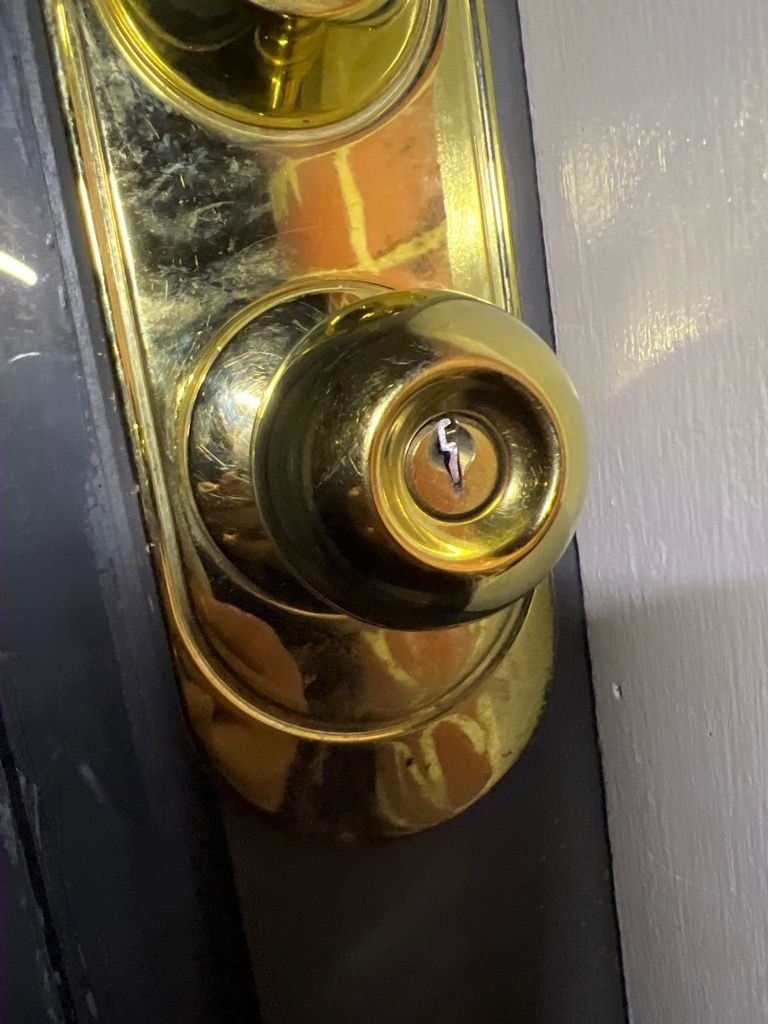 Close-up of a brass door lock with a broken key stuck in it on a white-painted door.