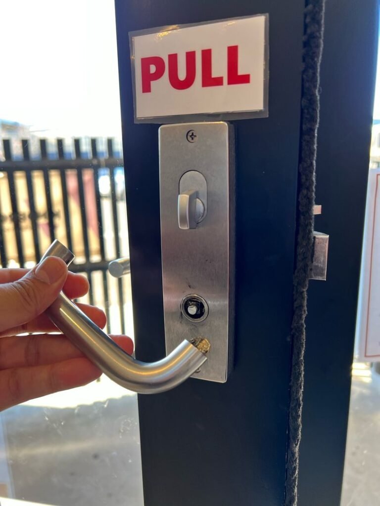 Hand holding a broken door handle next to a lock with a "PULL" sign above it.