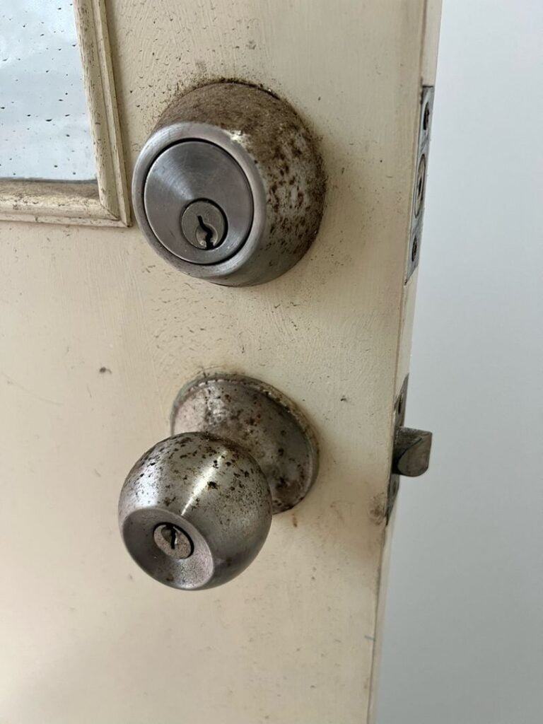 Old and rusted door lock and knob on a partially open door.