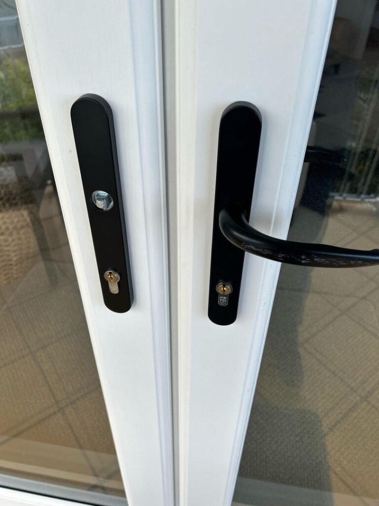 Close-up of a broken door lock handle on a white double door with black handles.