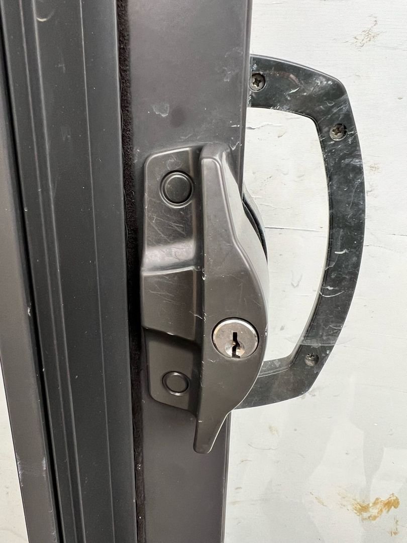 Close-up of a re-keyed sliding door lock with a keyhole and handle on a dark-colored frame.